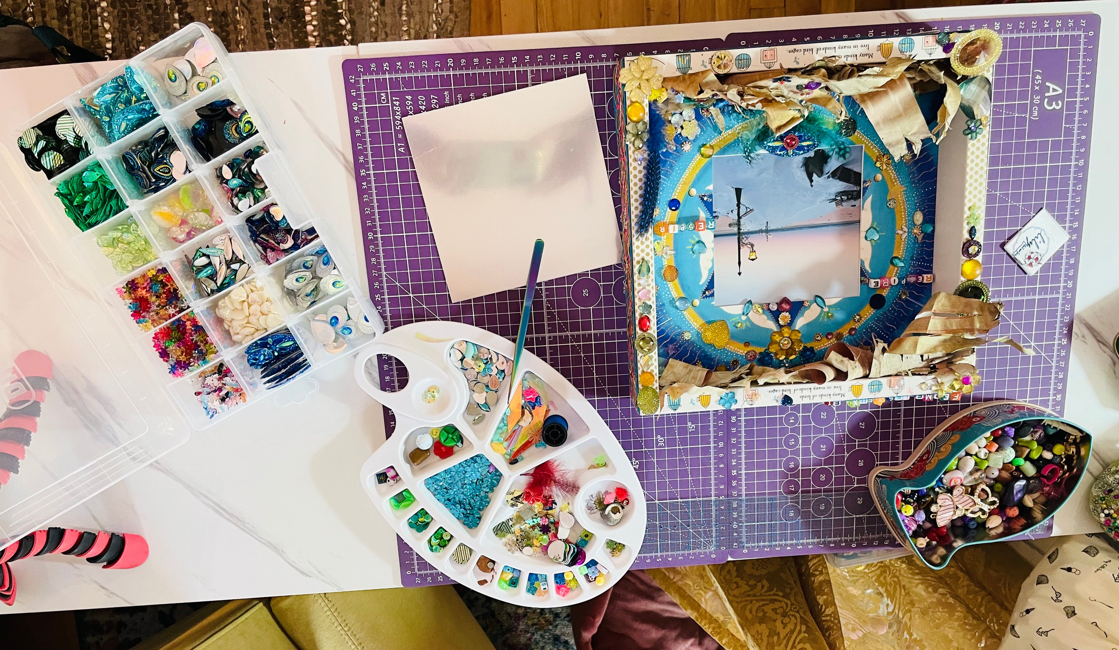 Vue d'ensemble du matériel de fabrication sur une table de travail : Perles, pompoms, sequins