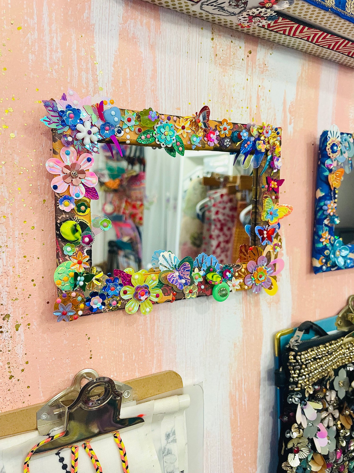 Miroir accessoirisé de sequins et paillettes sur un mur blanc et rose parmi d'autres cadres